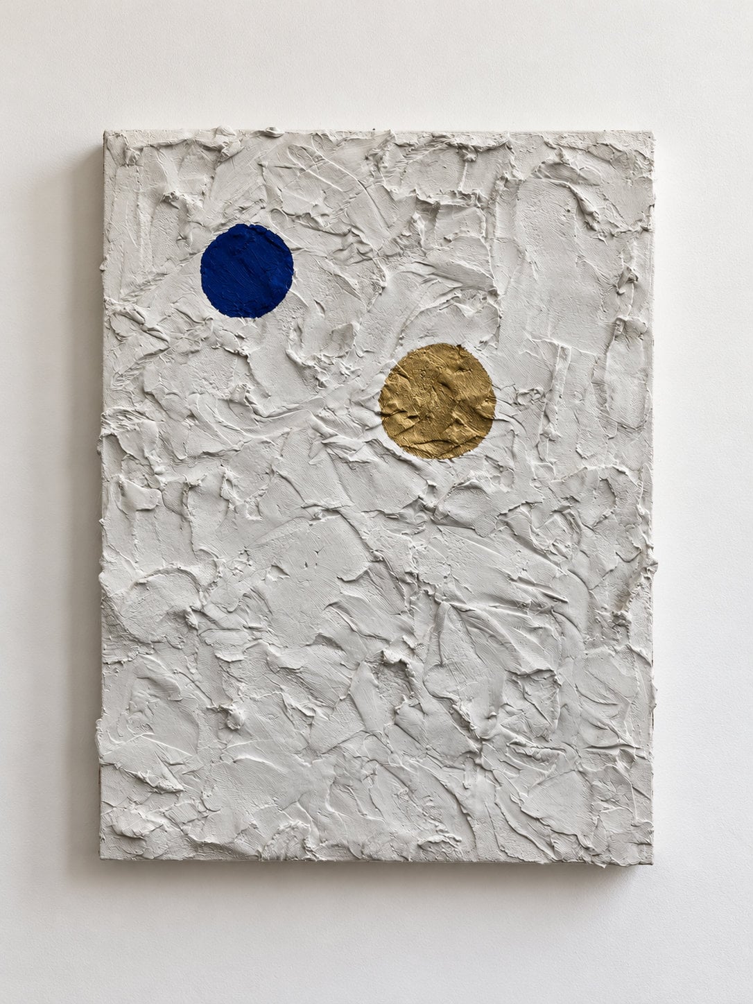 White plaster on canvas with a dark blue circle and a gold circle aligning