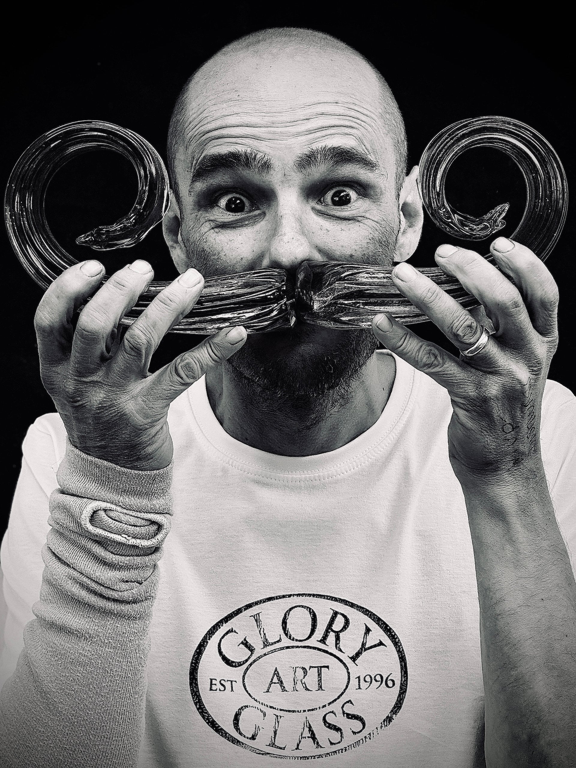 Black and white photo of a man holding glass moustache against his face