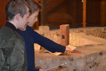 Two boys at newport roman villa with a clipboard and pointing at exhibits