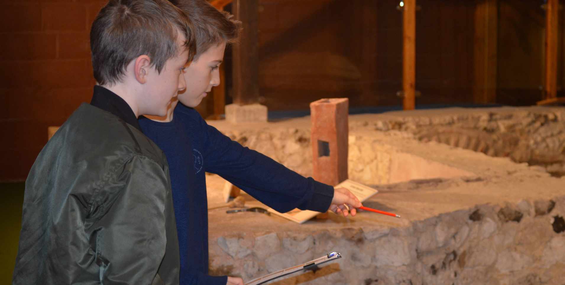 Two boys at newport roman villa with a clipboard and pointing at exhibits