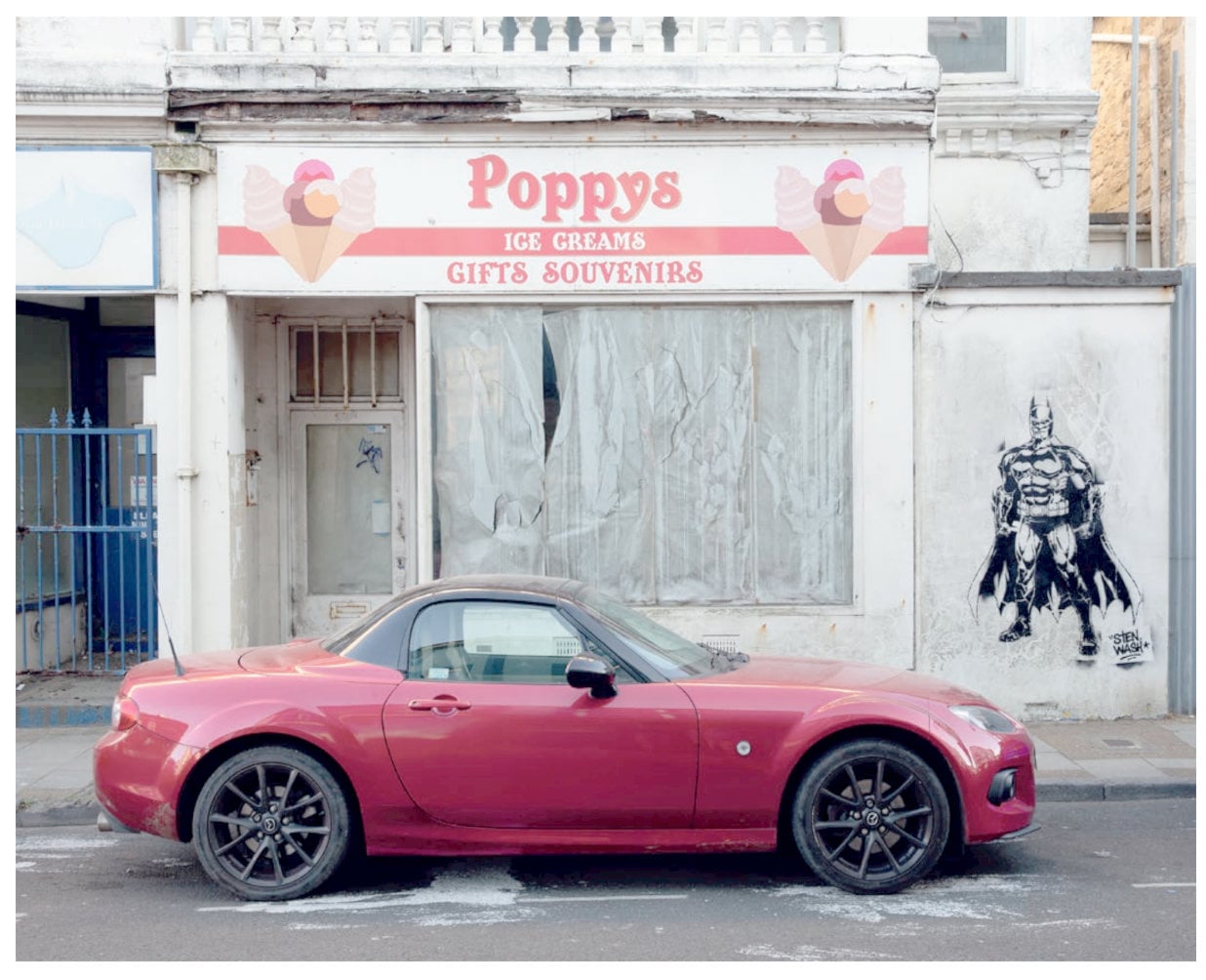 Red sports car outside a closed down ice cream shop, with batman stencilled graffiti art on the side door